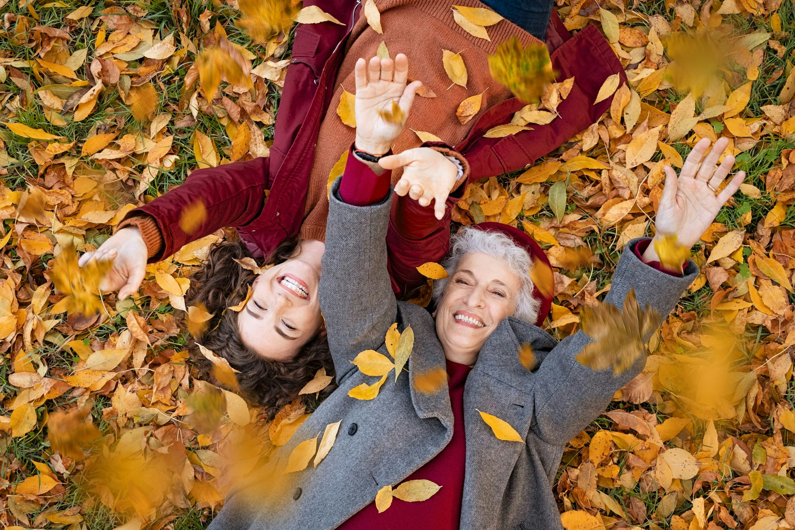 Grandmother and granddaughter lying on foliage and enjoy the autumn